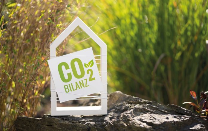 Weißes Haus im Garten mit Schild CO2 Bilanz