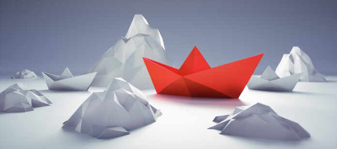 Rotes Papierschiff zwischen Eisbergen Die Verselbstständigung nicht performender Tochtergesellschaften oder Geschäftsbereiche. Der Carve-out als Instrument der Neuausrichtung.