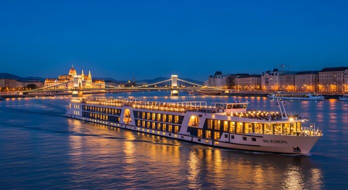Illuminated River Cruise Ship Navigates Danube River at Dusk in Budapest. Nachfolgebeteiligung bei 1AVista Reisen: VR Equitypartner steigt ein und stärkt Wachstum, Flottenausbau und Expansion im Kreuzfahrtmarkt.