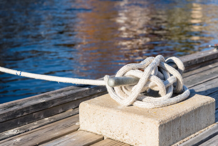 Close up of a mooring rope knotted to a cleat on a wooden pier in a harbour on a sunny autumn day. Selective focus.