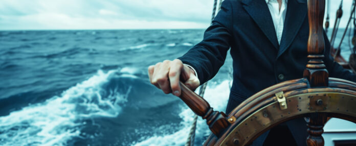 close up of hands on the wheel, young man in suit at helm of old wooden ship sailing through stormy sea, close-up. Business concept with copy space