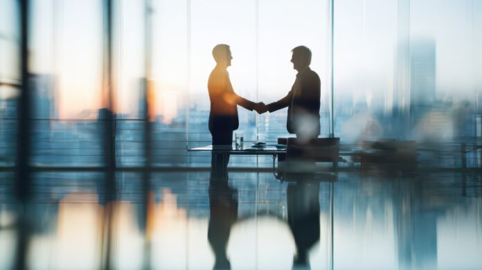 Two business professionals shake hands over a signed contract in a modern office, symbolizing a corporate merger and teamwork Oracle-KI: Abacus alpha übernimmt merlin.zwo und stärkt KI- und Datenbanklösungen für Mittelstand und öffentliche Kunden.
