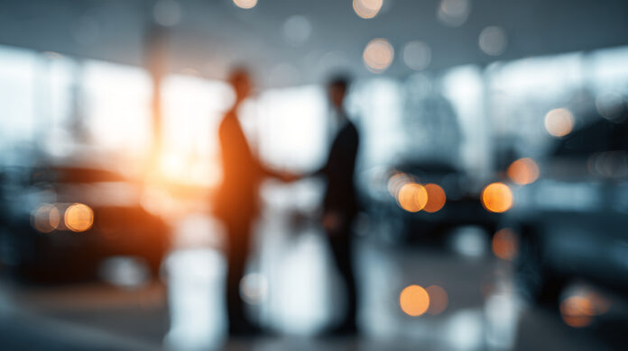 The image blurs as two people hold hands in a luxury car showroom, Concepts related to buying, selling, or leasing a car. Unternehmen im Mittelstand nutzen Sale & Lease Back, um Liquidität zu schaffen und finanzielle Spielräume zu erweitern.