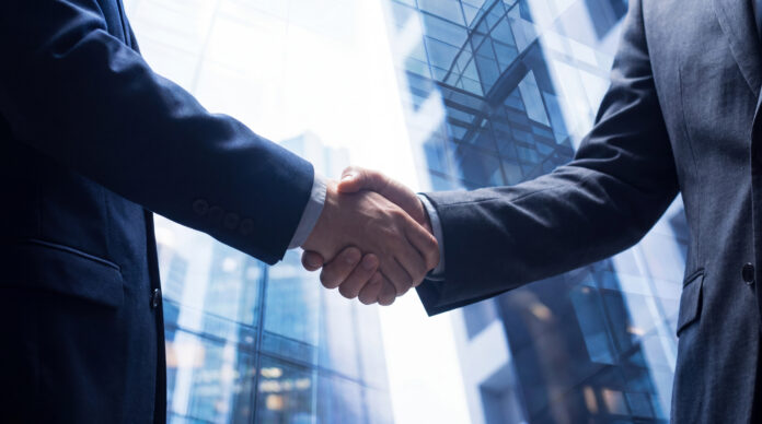 Two businessmen in suits shaking hands, symbolizing agreement with blurred corporate building. Auctus steigt als Mehrheitsinvestor bei LMX ein und legt damit den Grundstein für den Aufbau einer europäischen Touristikplattform.