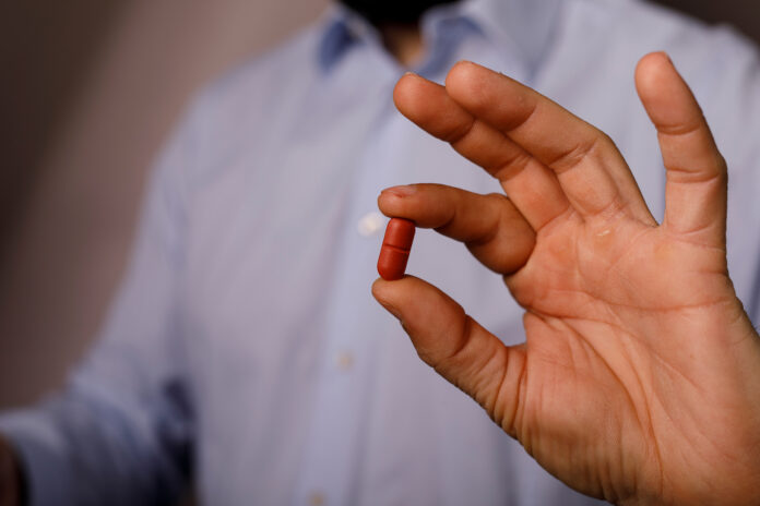 Close-up of a hand holding a red capsule medication for health.