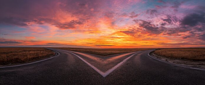Two diverging paths represent making a decision and finding a new direction, leading to opportunity under a colorful sky at dusk