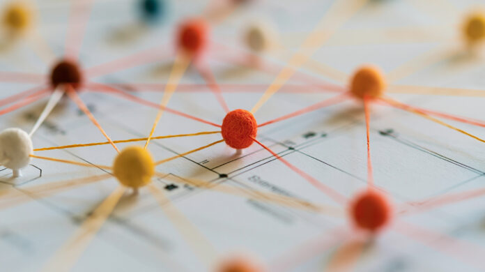 Colorful spheres connected by threads represent a complex data network on a blueprint. This illustrates global connectivity and abstract technology system concepts.